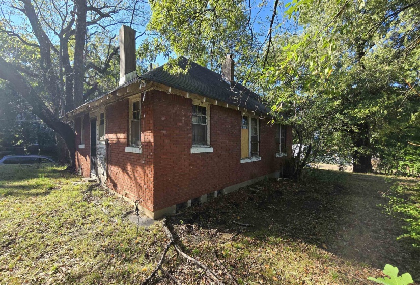 View of home's exterior featuring a chimney, brick siding, and a lawn
