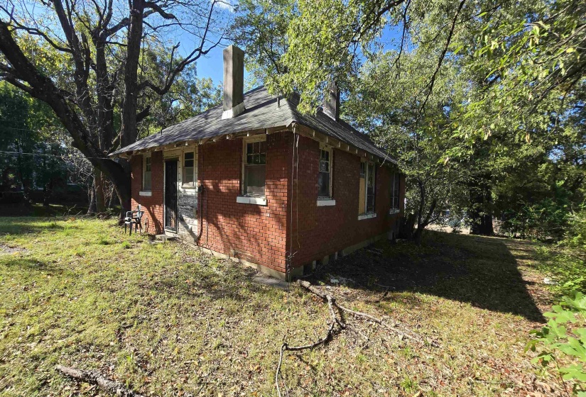 View of side of property featuring brick siding, a chimney, and a yard