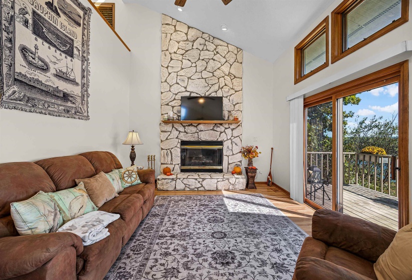 Living room with high vaulted ceiling, wood finished floors, a stone fireplace, and a ceiling fan