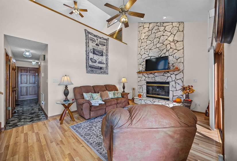 Living room with high vaulted ceiling, ceiling fan, a fireplace, and wood finished floors