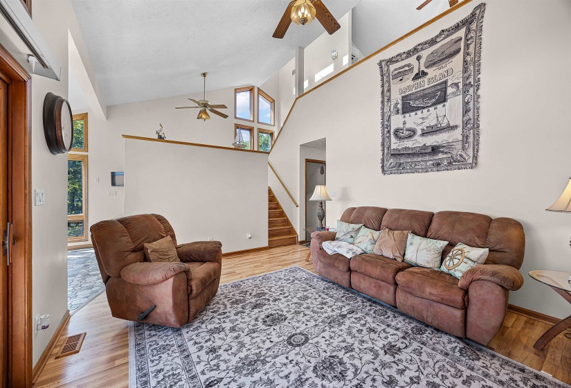 Living area featuring healthy amount of natural light, high vaulted ceiling, stairway, ceiling fan, and light wood-style flooring