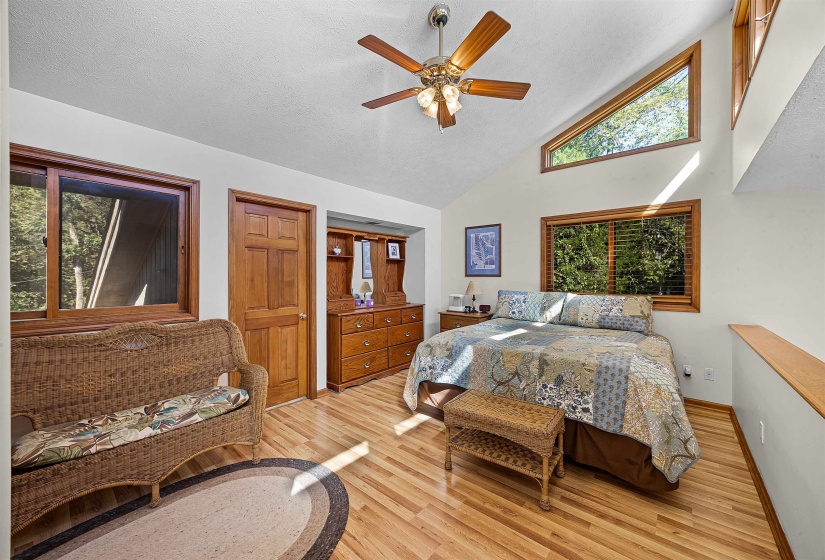 Bedroom with light wood-type flooring, high vaulted ceiling, ceiling fan, and a textured ceiling