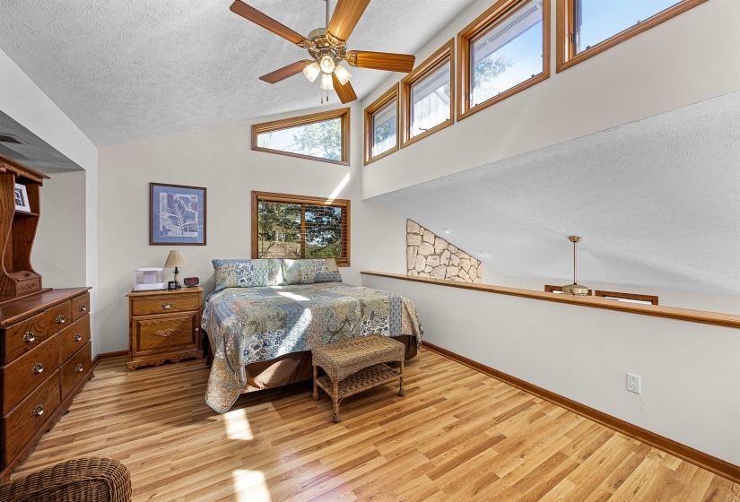 Bedroom with a textured ceiling, light wood-style floors, high vaulted ceiling, and ceiling fan