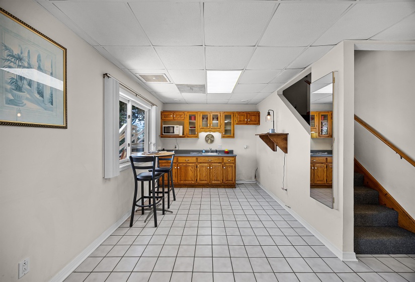 Bar area with brown cabinets, a drop ceiling, glass insert cabinets, light tile patterned floors, and stairs