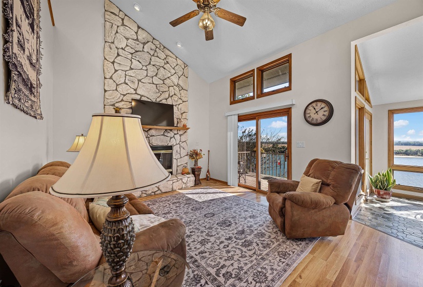 Living room featuring high vaulted ceiling, wood finished floors, a stone fireplace, a ceiling fan, and recessed lighting