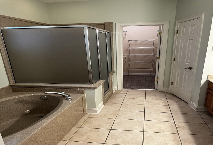 Bathroom featuring light tile patterned floors, a shower stall, vanity, a tub with jets, and a walk in closet