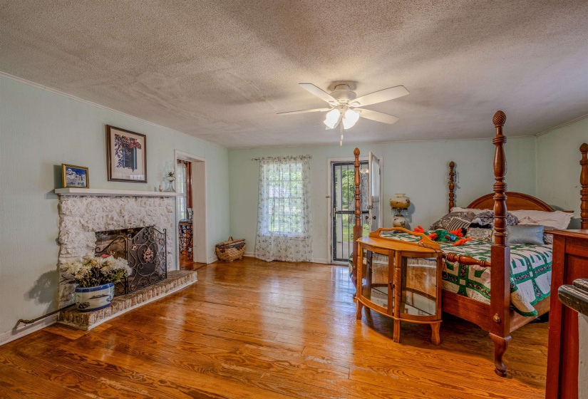 Bedroom featuring a textured ceiling, wood finished floors, access to exterior, a fireplace, and baseboards