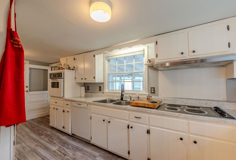 Kitchen with white appliances, under cabinet range hood, a sink, white cabinetry, and a textured ceiling