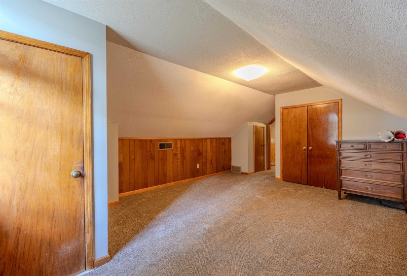 Bonus room featuring lofted ceiling, carpet, baseboards, a textured ceiling, and wooden walls