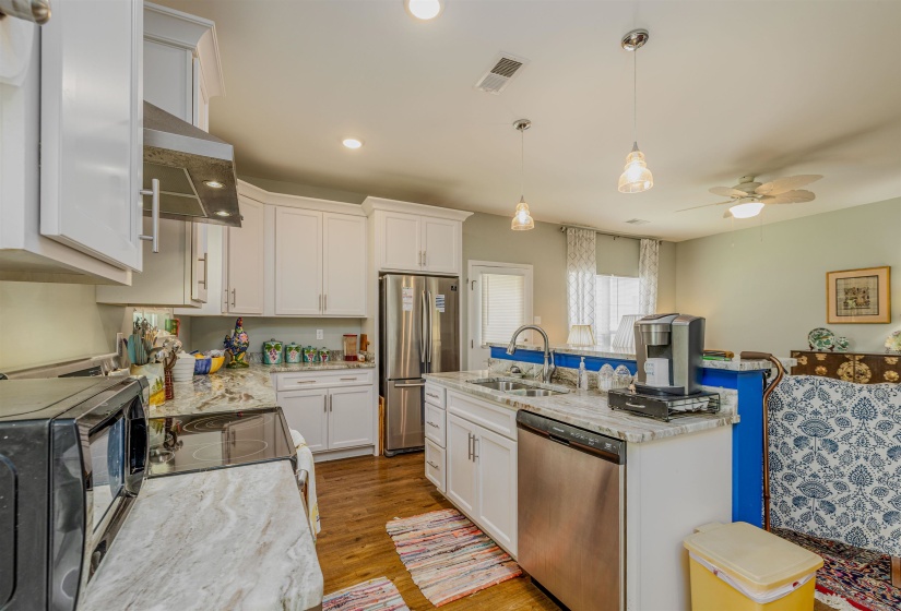 Kitchen with stainless steel appliances, range hood, a sink, a kitchen island with sink, and white cabinetry