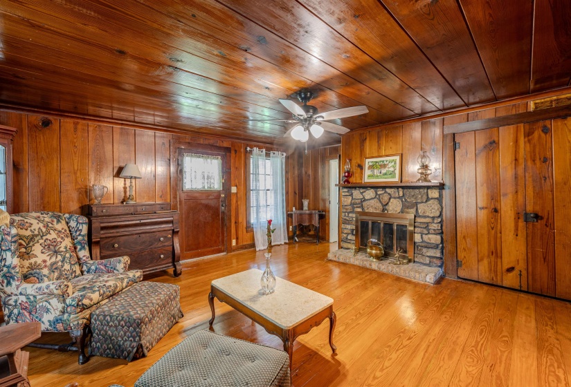 Living room featuring wooden ceiling, wood walls, wood finished floors, ceiling fan, and a fireplace