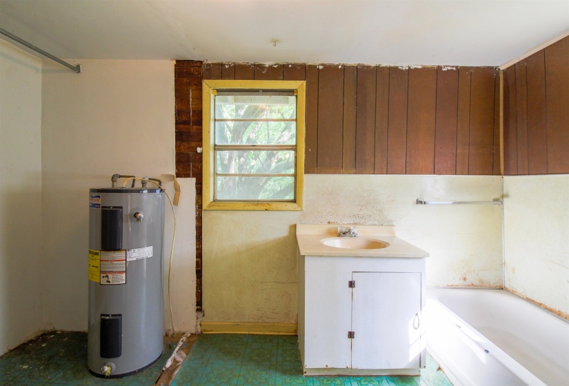 Bathroom with a bath, electric water heater, dark floors, and vanity