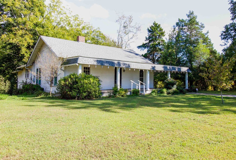 View of side of property featuring covered porch, a chimney, a lawn, and a shingled roof