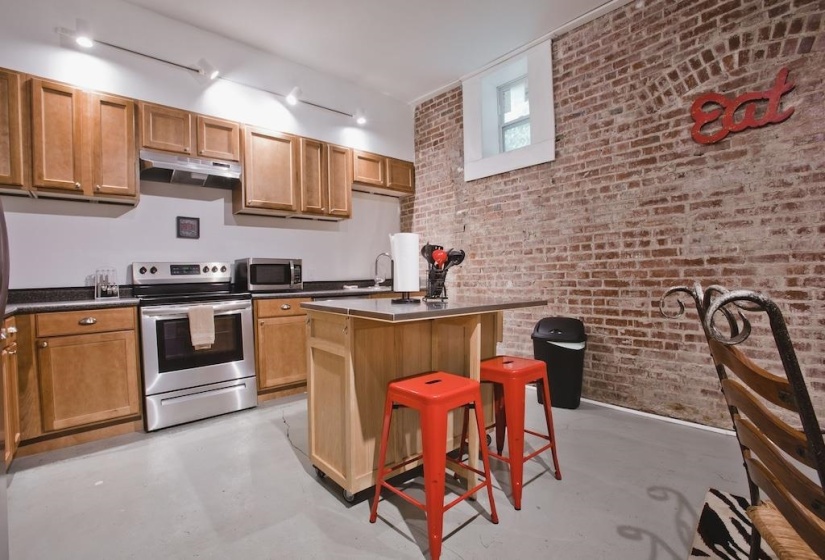 Kitchen with brick wall, appliances with stainless steel finishes, finished concrete flooring, a breakfast bar area, and under cabinet range hood