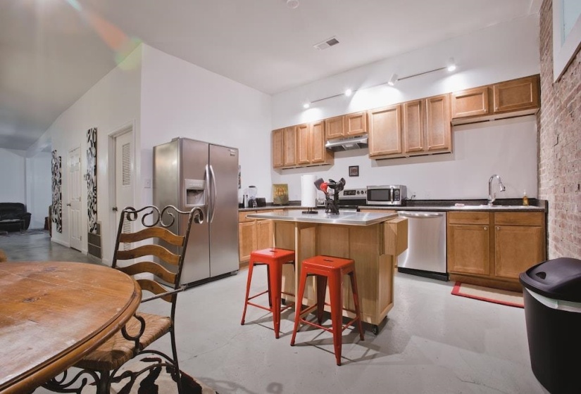Kitchen with stainless steel appliances, a breakfast bar area, a kitchen island, under cabinet range hood, and finished concrete flooring