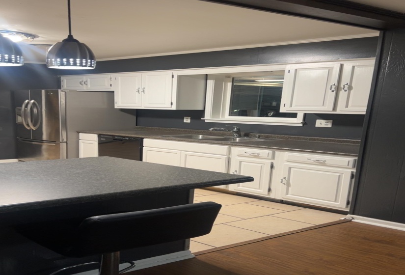 Kitchen with crown molding, white cabinetry, dark countertops, light wood-style floors, and black dishwasher
