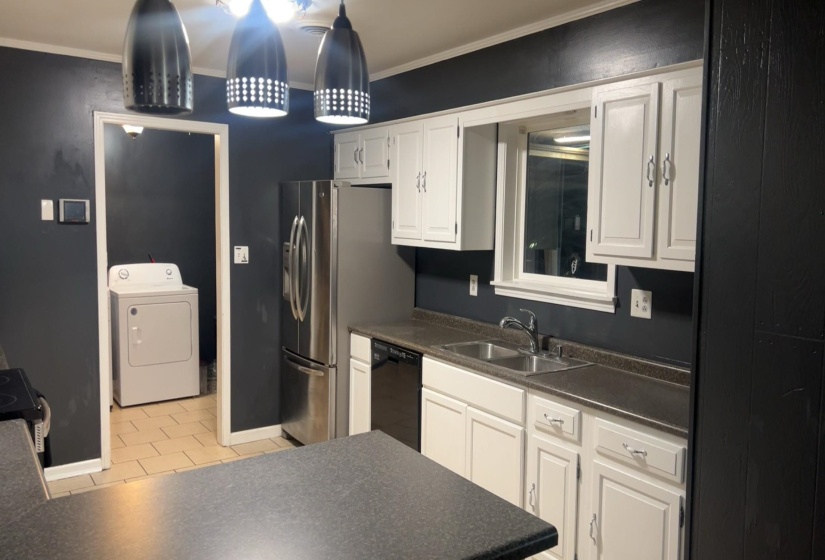 Kitchen featuring dark countertops, white cabinets, washer / dryer, ornamental molding, and light tile patterned floors