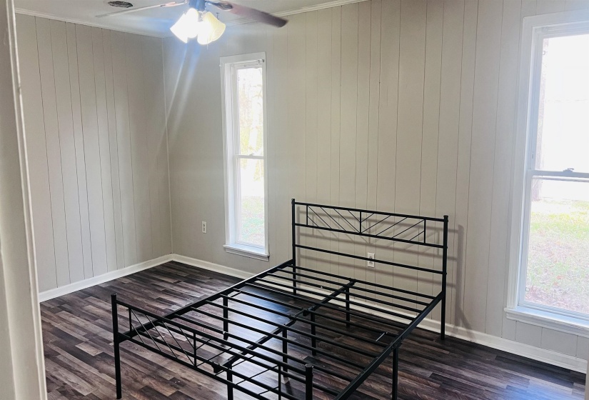 Unfurnished bedroom with wood walls, dark wood-type flooring, ornamental molding, and a ceiling fan