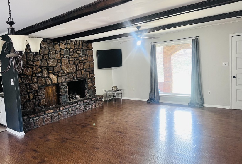 Unfurnished living room with dark wood-style floors, a stone fireplace, beam ceiling, and ceiling fan
