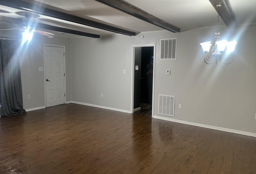 Unfurnished room with a chandelier, beam ceiling, and dark wood-style floors