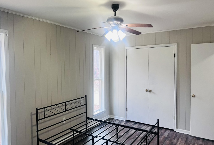 Unfurnished bedroom featuring wood walls, dark wood-type flooring, a ceiling fan, and a closet