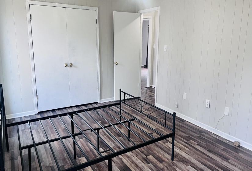 Unfurnished bedroom featuring wooden walls, dark wood finished floors, and a closet