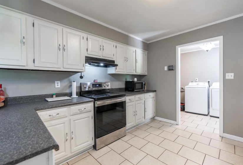 Kitchen featuring electric range, white cabinets, ornamental molding, and dark countertops