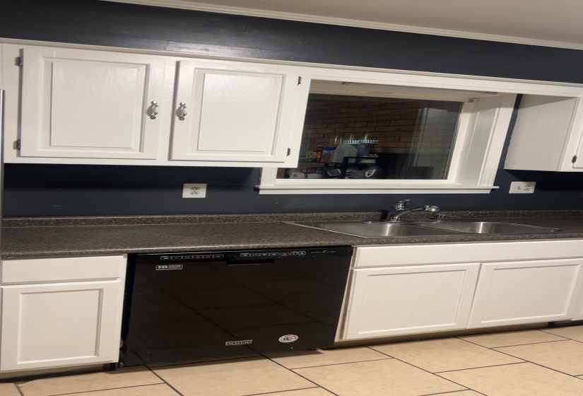 Kitchen featuring white cabinets, dark countertops, black dishwasher, and light tile patterned floors