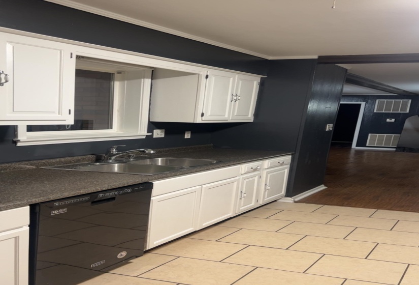 Kitchen featuring dark countertops, white cabinets, dishwasher, crown molding, and light tile patterned floors