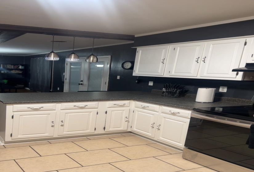 Kitchen featuring white cabinets, stainless steel electric stove, a peninsula, dark countertops, and hanging light fixtures