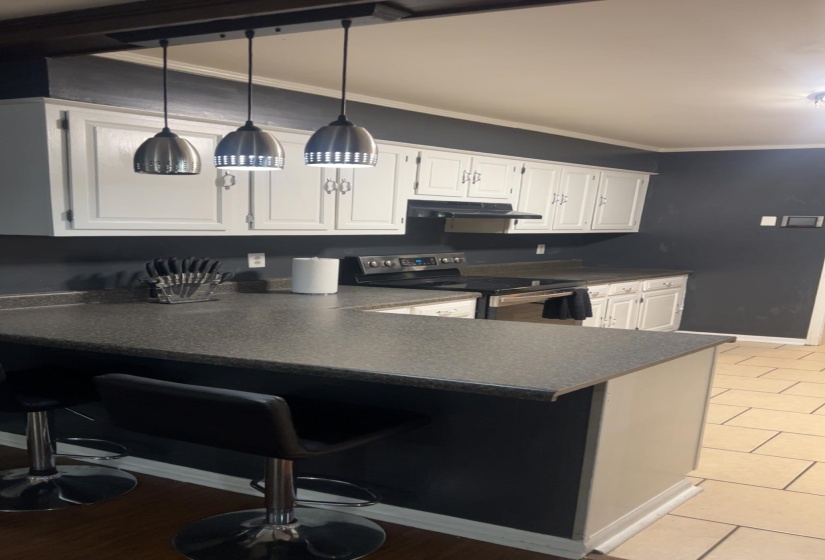 Kitchen featuring dark countertops, stainless steel range with electric stovetop, a kitchen breakfast bar, decorative light fixtures, and crown molding