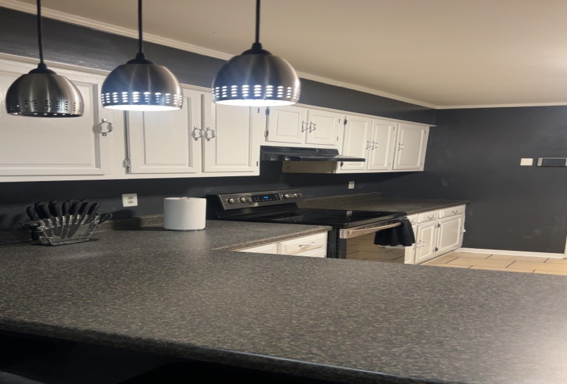 Kitchen featuring stainless steel electric range oven, white cabinetry, crown molding, decorative light fixtures, and under cabinet range hood