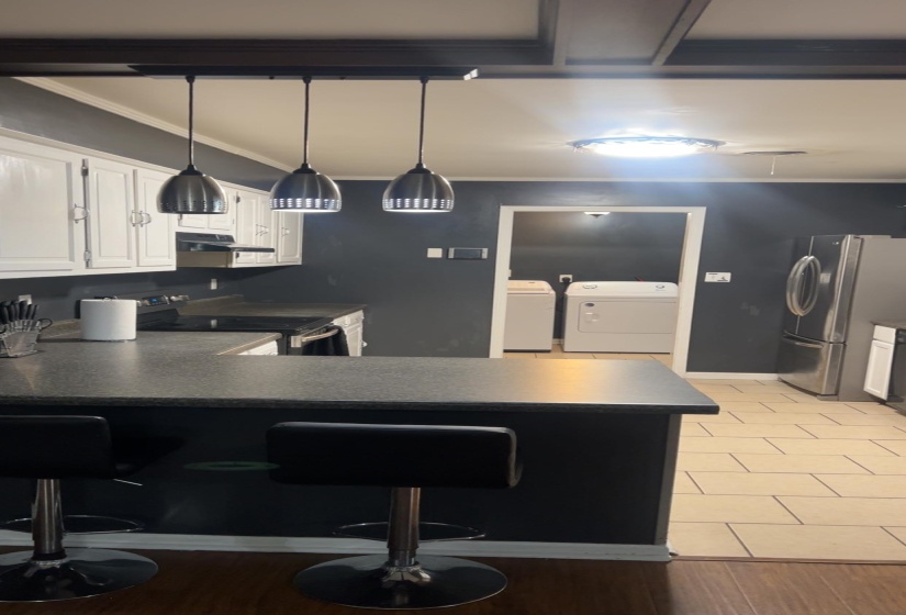 Kitchen with dark countertops, appliances with stainless steel finishes, a kitchen breakfast bar, white cabinets, and hanging light fixtures
