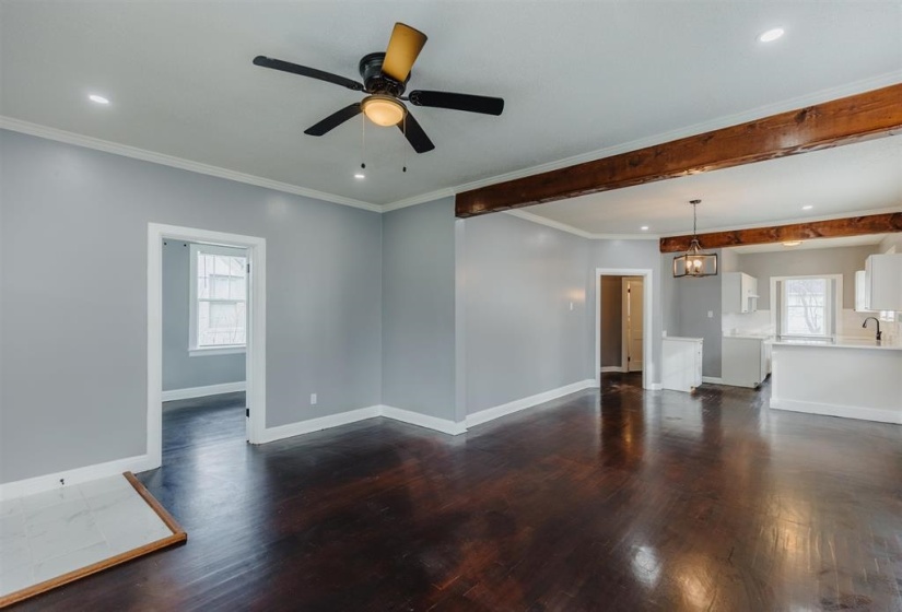 Unfurnished living room with sink, ceiling fan with notable chandelier, crown molding, and dark wood-type flooring