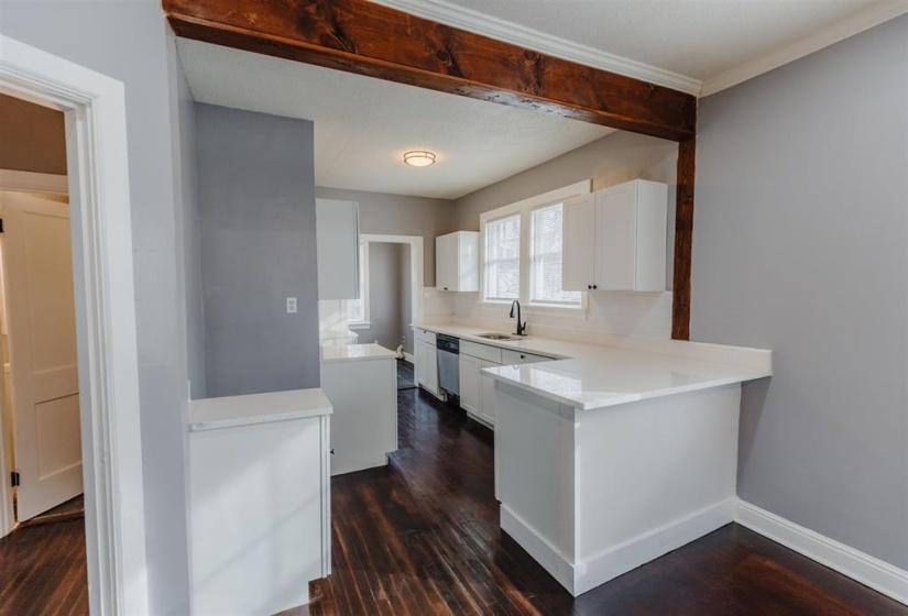 Kitchen featuring stainless steel dishwasher, sink, dark hardwood / wood-style flooring, white cabinetry, and ornamental molding