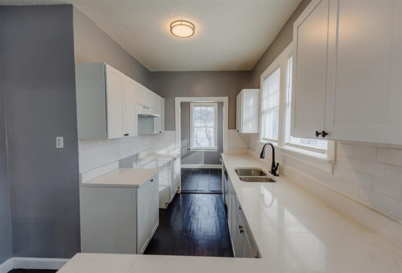 Kitchen with dark wood-type flooring, white cabinets, sink, and decorative backsplash
