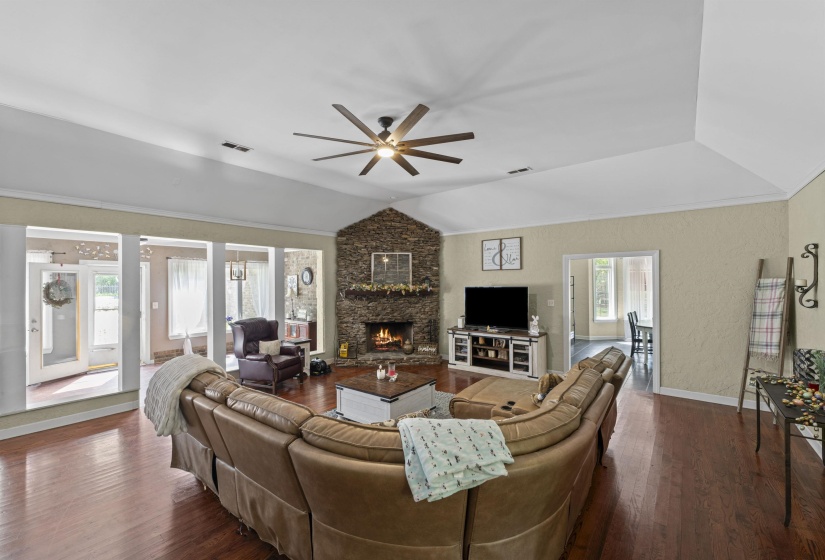 Living area with lofted ceiling, a ceiling fan, a stone fireplace, and dark wood-style floors