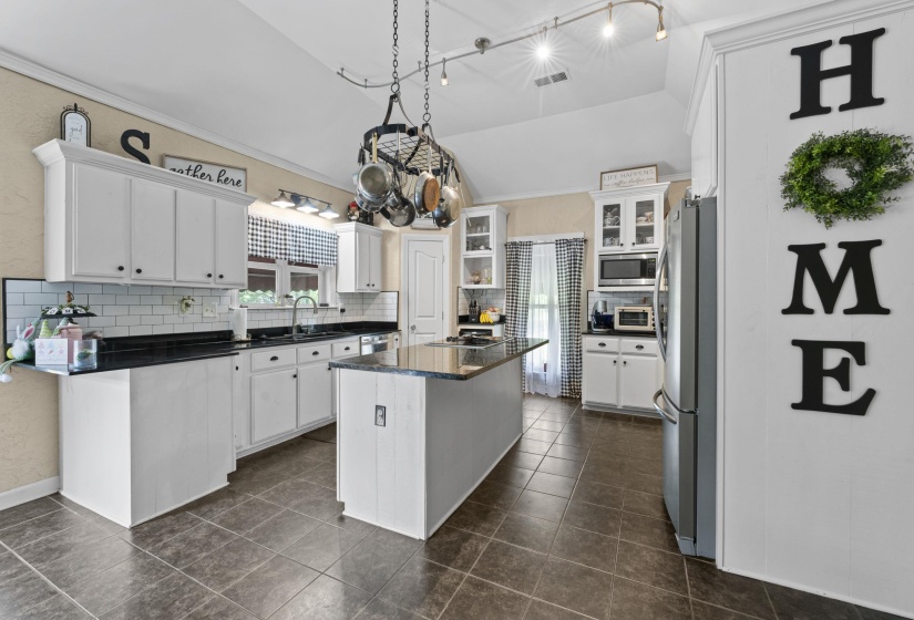 Kitchen featuring stainless steel appliances, vaulted ceiling, a sink, and dark countertops