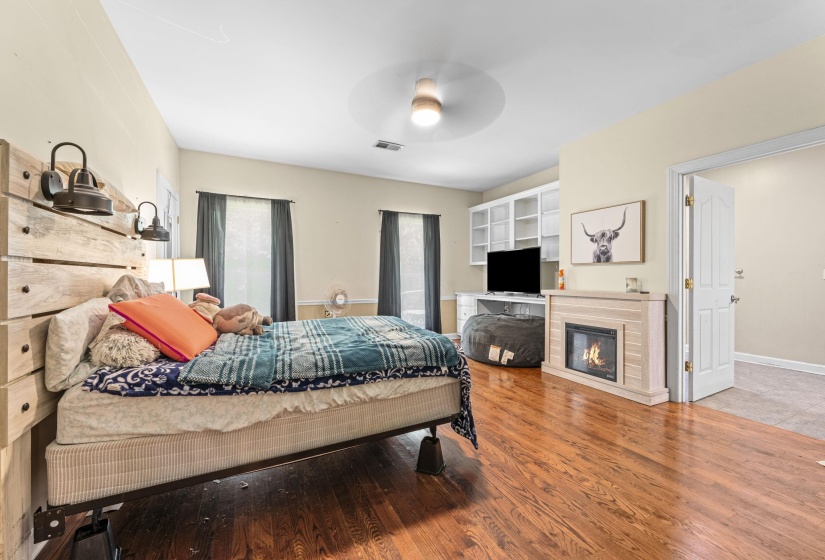 Bedroom featuring wood finished floors, visible vents, a ceiling fan, baseboards, and a glass covered fireplace