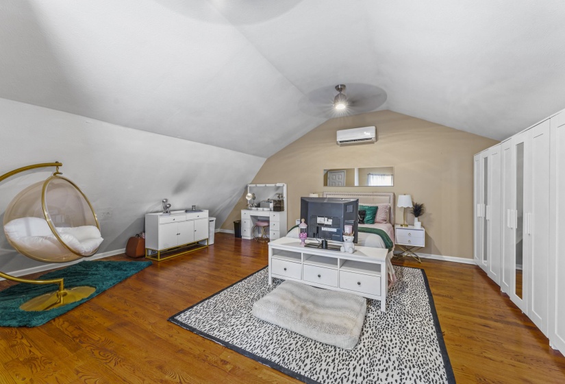 Bedroom featuring baseboards, lofted ceiling, wood finished floors, and a wall unit AC