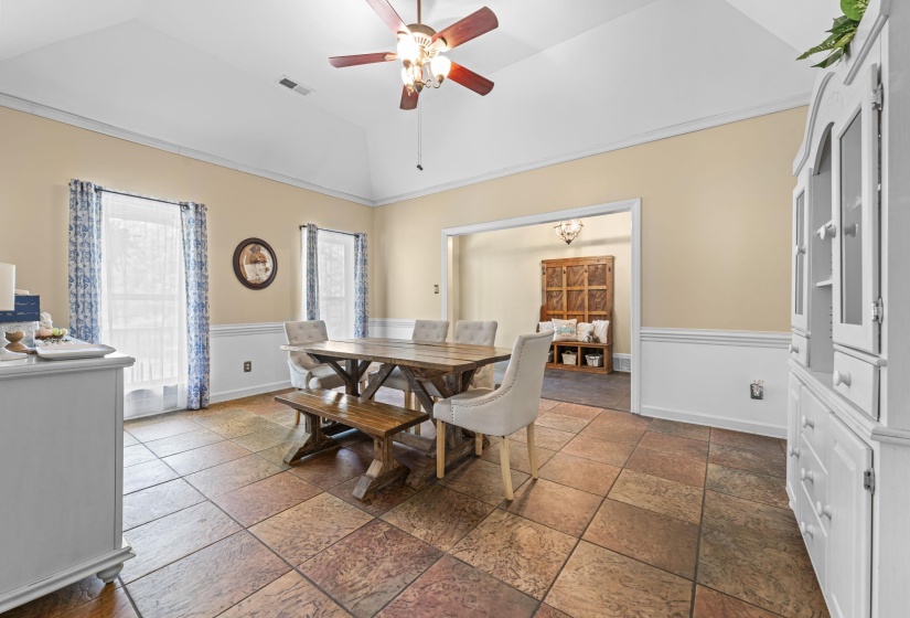 Dining area featuring a ceiling fan, stone tile floors, a wainscoted wall, lofted ceiling, and visible vents