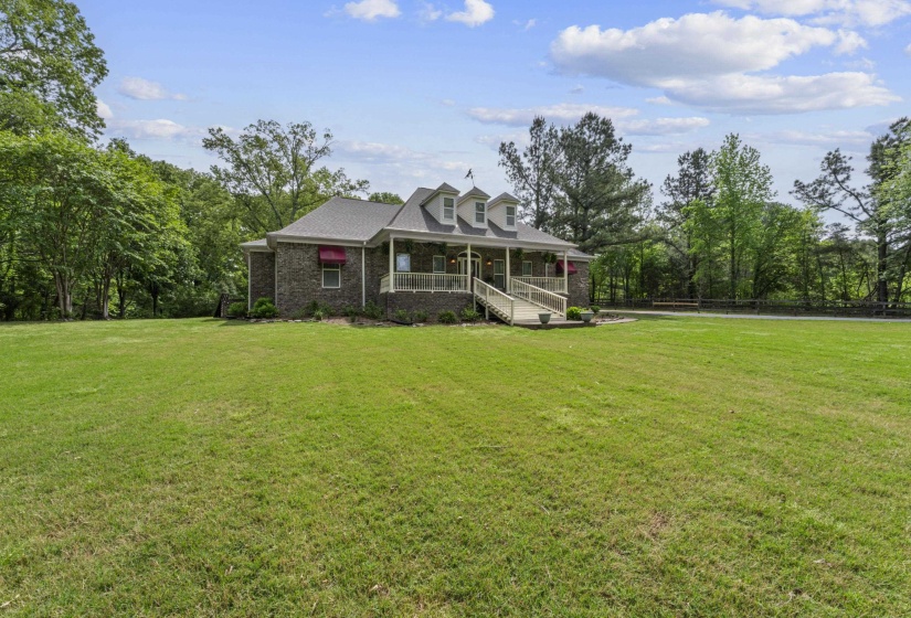 View of front facade with brick siding, a front lawn, covered porch, and fence