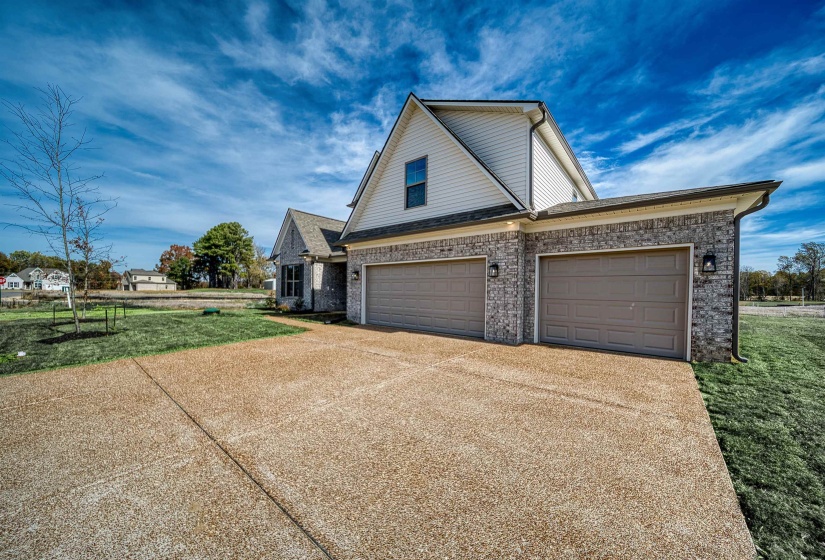 View of side of property featuring a lawn, concrete driveway, and brick siding