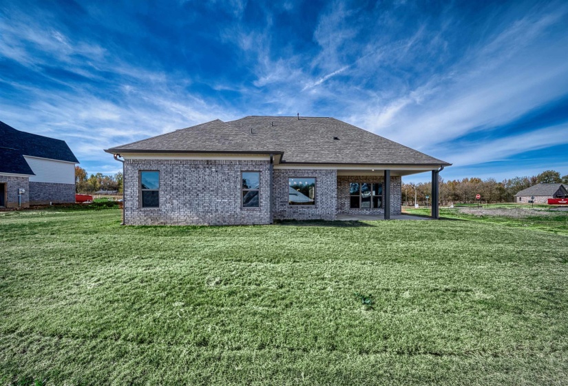 Rear view of property featuring brick siding, a patio area, a shingled roof, and a lawn