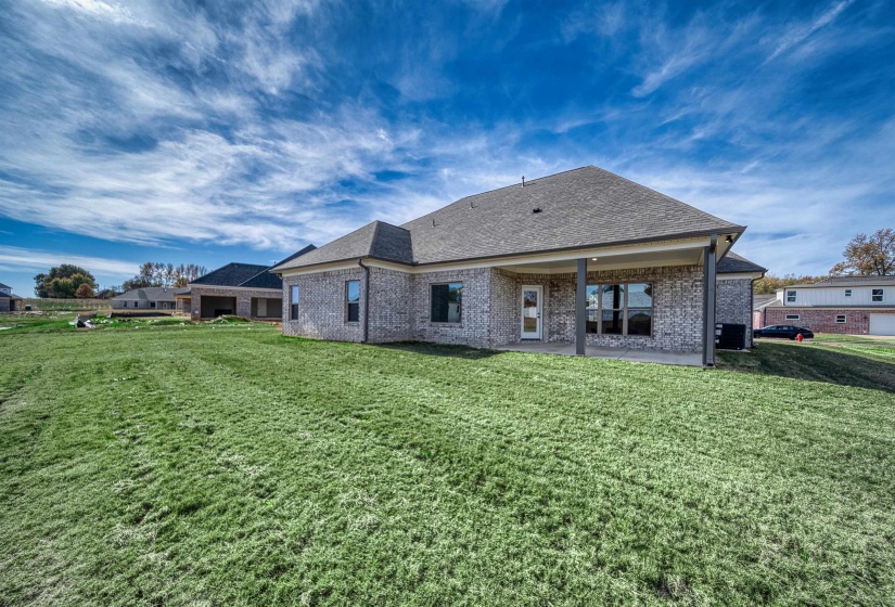 Rear view of property featuring a patio area, roof with shingles, brick siding, and a lawn