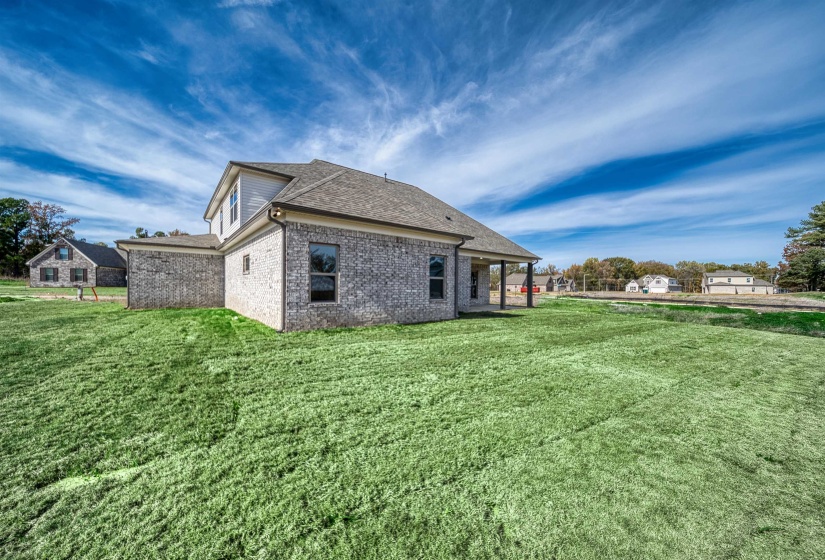 Rear view of house featuring brick siding, a patio, roof with shingles, and a yard