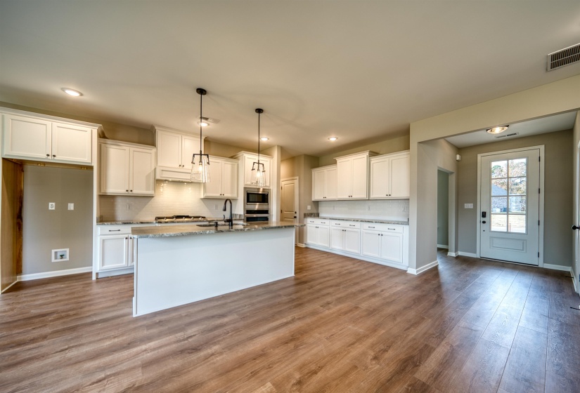 Kitchen with backsplash, white cabinetry, dark wood-style floors, pendant lighting, and a center island with sink