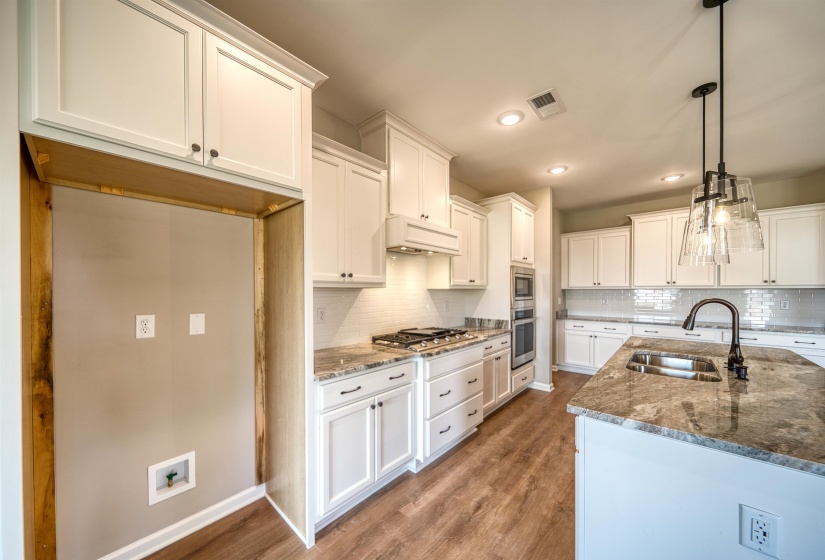 Kitchen featuring dark stone countertops, white cabinets, decorative light fixtures, dark wood finished floors, and custom range hood