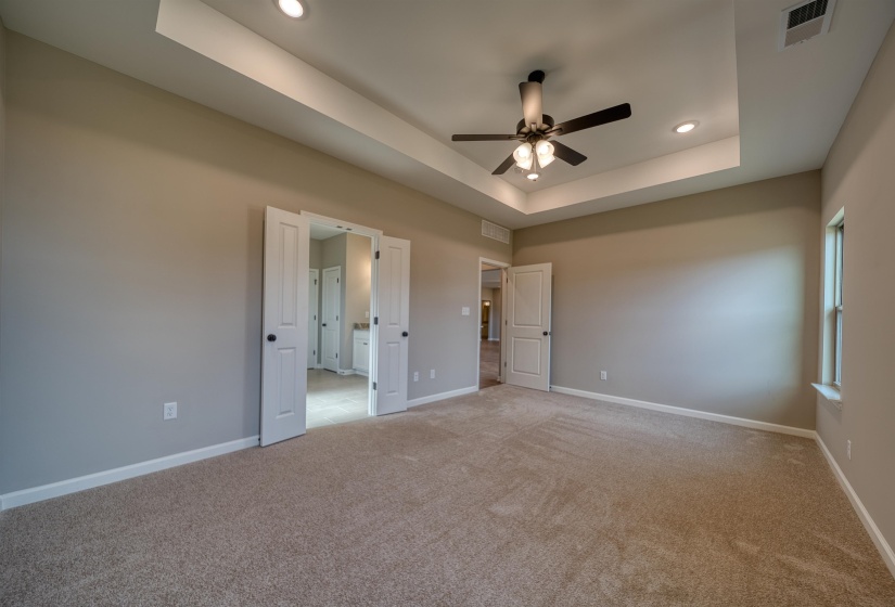 Unfurnished bedroom with a tray ceiling, light colored carpet, ceiling fan, and recessed lighting