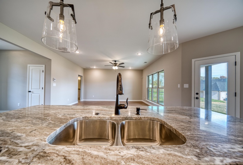 Kitchen view of recessed lighting, ceiling fan, light stone countertops, hanging light fixtures, and a chandelier